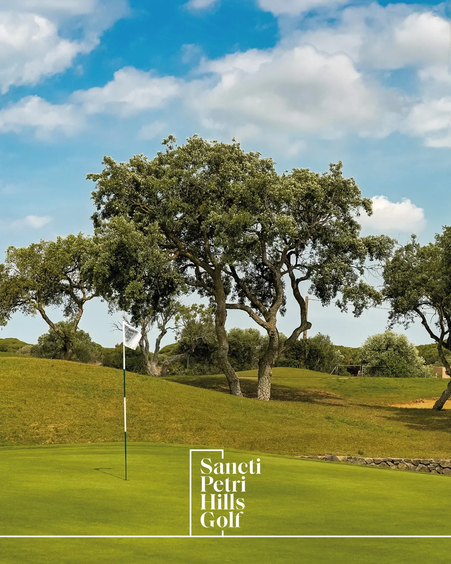 Green y bandera del campo de Manuel Piñero en Sancti Petri Hills Golf entre alcornoques y cielo azul de Chiclana